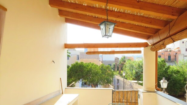 A balcony with a wooden table and bench, a hanging lantern, and a view of greenery and buildings. - mivigio dual use (Lipari)