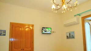 A room with a wooden wardrobe, a television mounted on the wall, a small wooden desk, and a patterned chair. - mivigio dual use (Lipari)