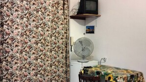 A small room with a patterned curtain, a television on a shelf, a fan, a table with a floral tablecloth, and a sofa. - economy central chamber (Lipari)