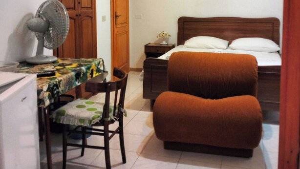 A bedroom with a bed, a chair, a desk with a fan, a painting on the wall, and a ceiling fan. - economy central chamber (Lipari)