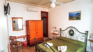A bedroom with a bed, a wooden wardrobe, a desk, a chair, a red trash bin, a ceiling fan, and a framed picture on the wall. - Standard room (Lipari)