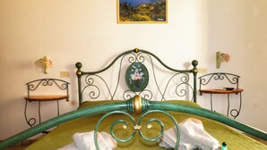 A bed with green metal headboard and footboard, two bedside tables, and a framed picture on the wall. - Standard room (Lipari)