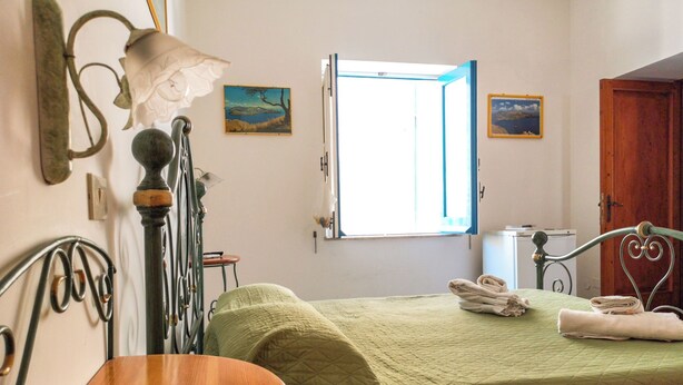 A room with a bed, a table, a lamp, and a window with a view of the outdoors. - Standard room (Lipari)