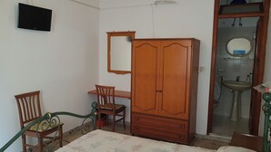 A bedroom with a wooden wardrobe, a desk, a chair, a bed, and a bathroom visible through an open door. - Standard room (Lipari)
