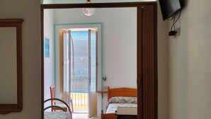 A room with a bed, a table with a remote control, a television on the wall, and a door leading to a balcony. - Deluxe Double (Lipari)