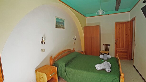 A bedroom with a bed, a wooden nightstand, a chair, a wardrobe, and a picture on the wall. - double use room on the street floor (Lipari)