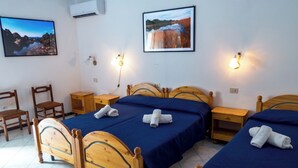 A hotel room with two wooden beds, a small wooden table, a chair, and a wall-mounted air conditioner. - Double Comfort (Lipari)