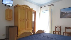A bedroom with a bed, wooden wardrobe, a small cabinet, two chairs, a television, and a painting on the wall. - Double Comfort (Lipari)