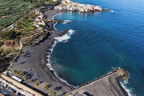 An aerial view of a coastal town with a beach, rocky shoreline, and buildings along the coast.