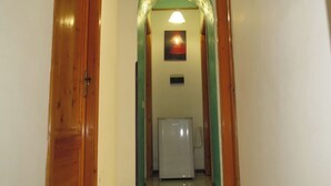 Un pasillo estrecho con puertas de madera a ambos lados, piso de baldosas y un refrigerador en el centro.
