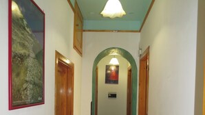 Un pasillo estrecho con puertas de madera, piso de baldosas y una lámpara en el techo.