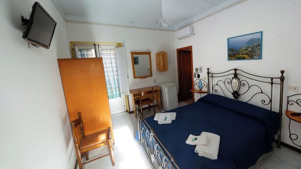 Une chambre à coucher avec un lit, un bureau, une chaise, un téléviseur et un tableau accroché au mur.
