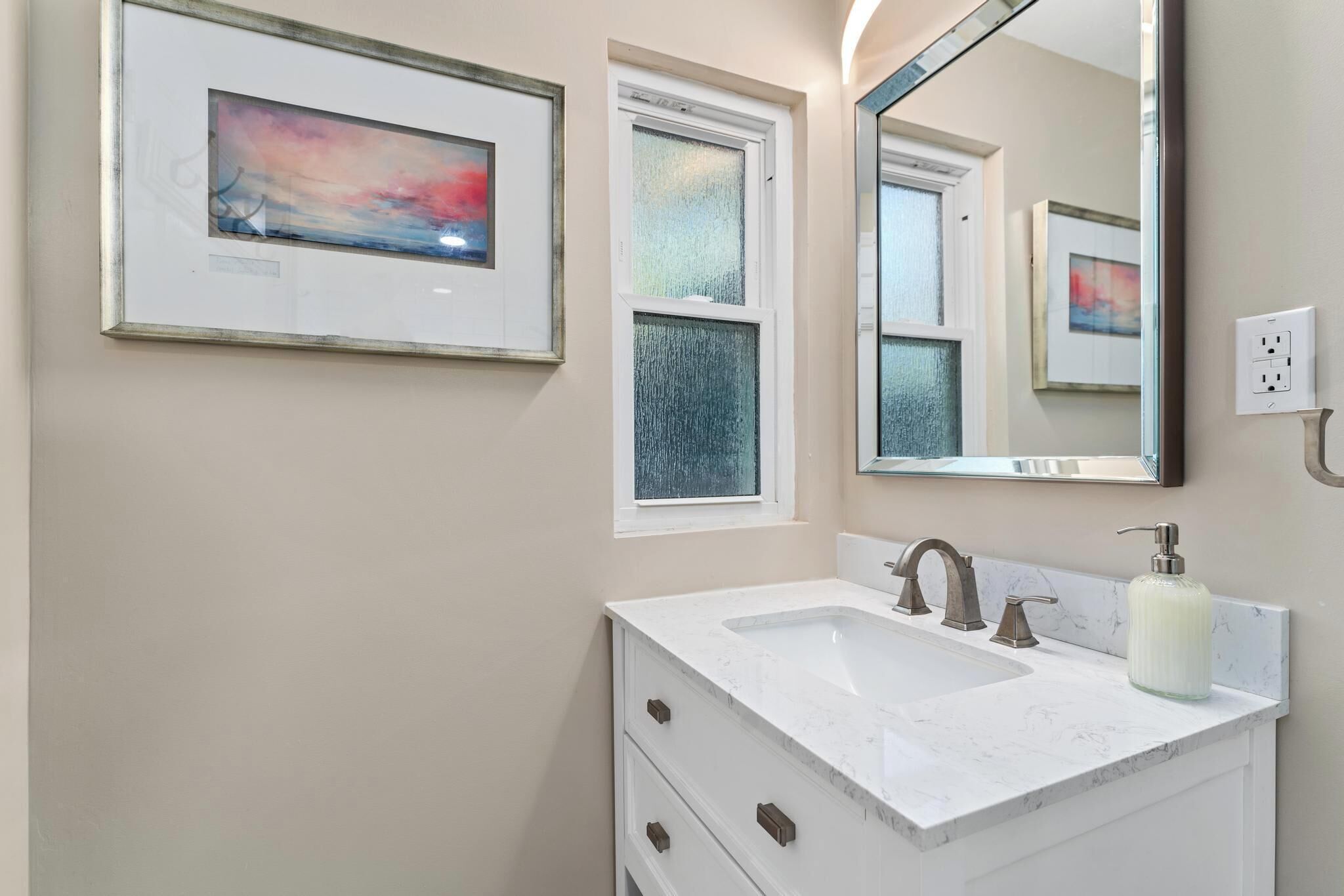 Een badkamer met een witte wastafel, een grote spiegel en twee ingelijste kunstwerken aan de muur.