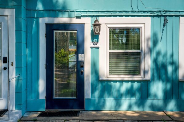 Una casa color turquesa con una puerta azul oscuro, una ventana con persianas y un pequeño porche.