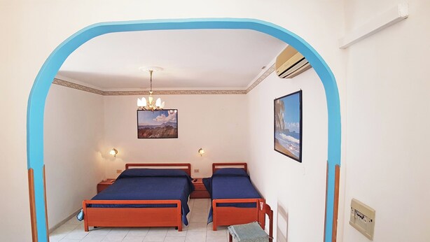 A bedroom with two beds, a chandelier, wall-mounted lights, and two framed pictures.