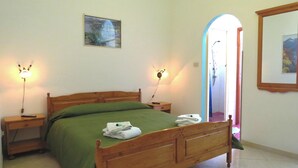 Une chambre à coucher avec un lit en bois, une literie verte, deux lampes de chevet, un tableau encadré au mur et une salle de bain visible à travers une arche.