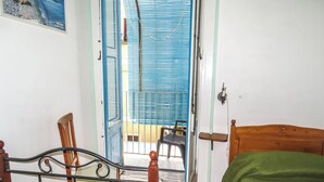 Une chambre avec un lit, une chaise, une table et un balcon avec des volets bleus.