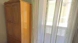 Une pièce avec une armoire en bois, une fenêtre équipée de stores verticaux et un sol carrelé.