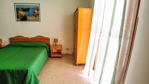Une chambre à coucher avec un lit, une armoire en bois, une table de chevet, une lampe, un tableau au mur et une fenêtre avec des rideaux.