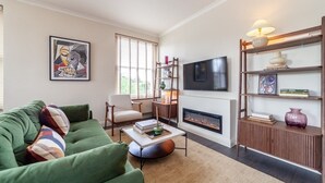 Un salon avec un canapé vert, une cheminée, un téléviseur et une bibliothèque.