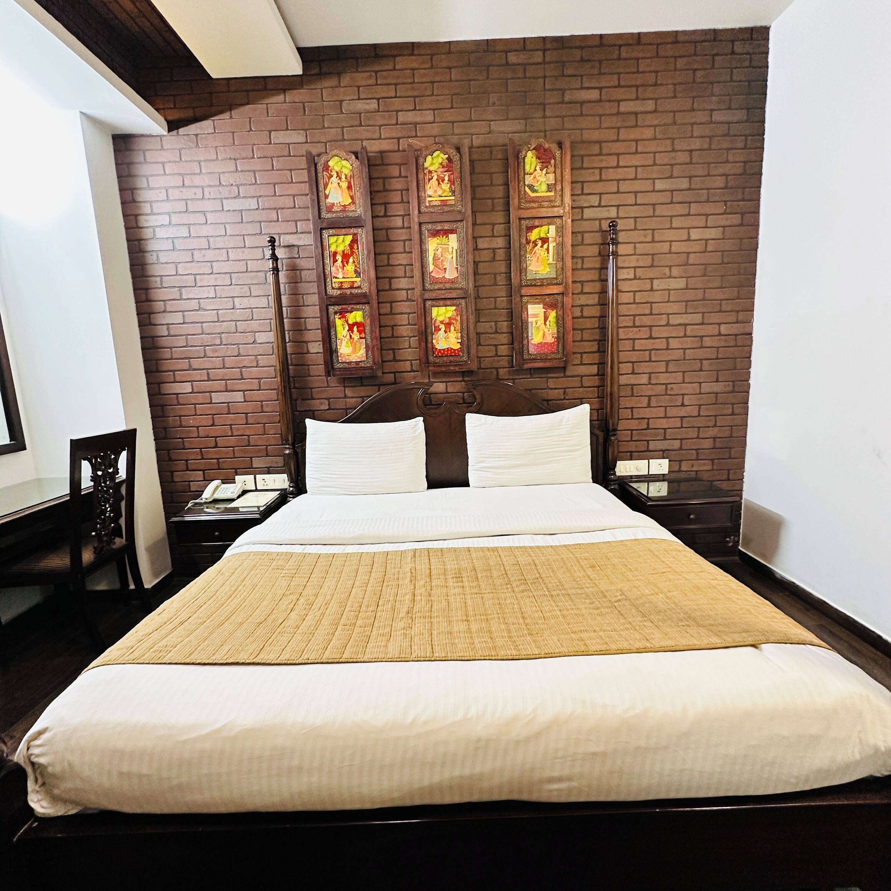 Habitación de hotel con pared de ladrillo, cama con ropa blanca y mesita de noche con teléfono.