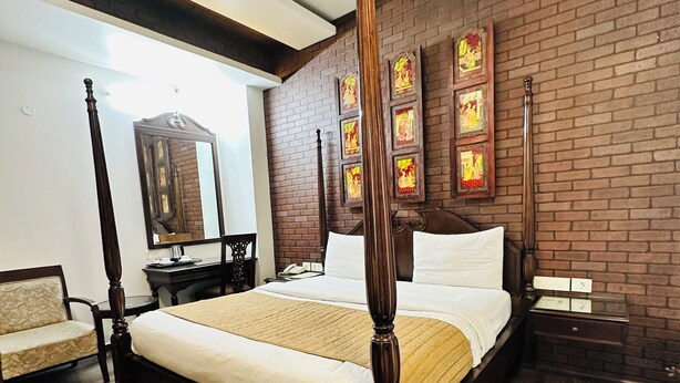 A four-poster bed with a wooden frame, a large mirror, and a brick wall with framed artwork. - Qotel Signature Lavish Inn Rajouri Garden (New Delhi)