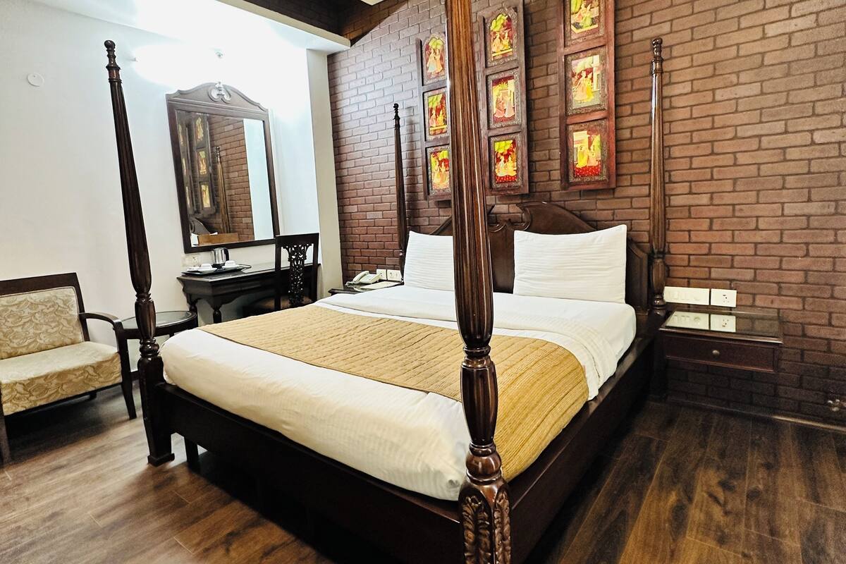 A four-poster bed with a wooden frame, a large mirror, and a brick wall with framed artwork.
