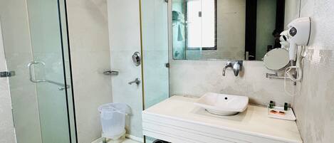 Un baño moderno con ducha cubierta por vidrio, lavamanos blanco y espejo grande.