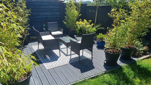 A patio area with a table and chairs, surrounded by potted plants and a wooden fence. - 1-bed Apartment - Sleeps 2 & Private Parking (Llansantffraid-ym-Mechain)