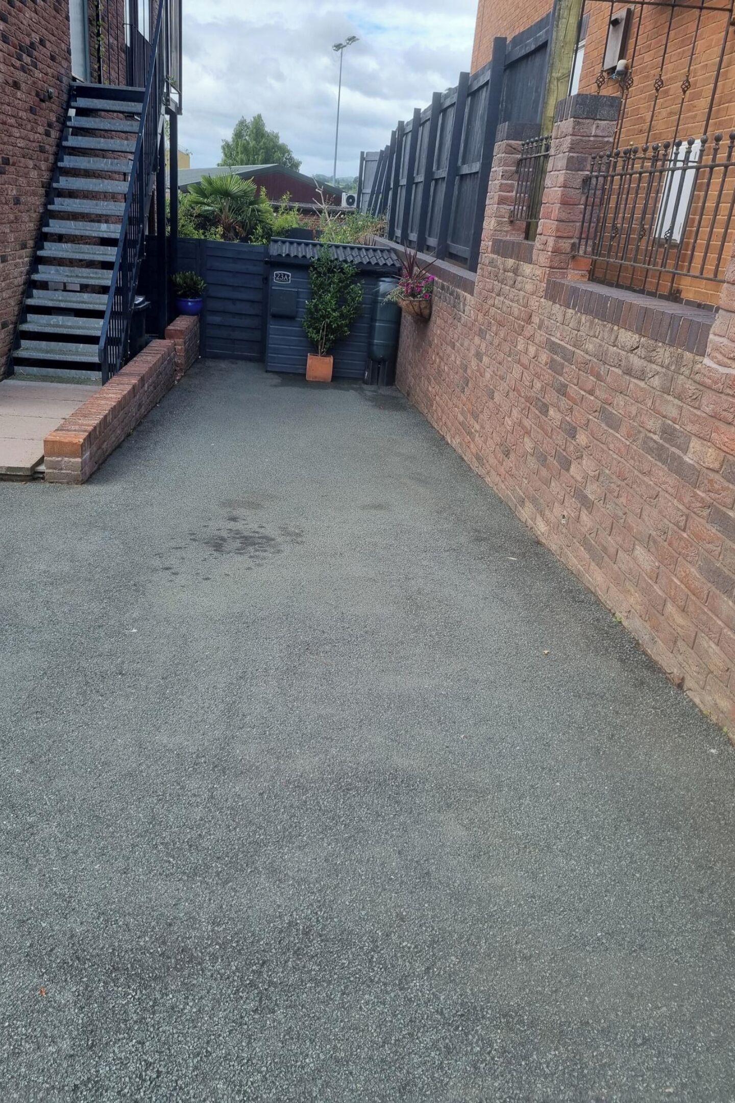 Un patio empedrado con un muro de ladrillo, una escalera de metal y una valla.