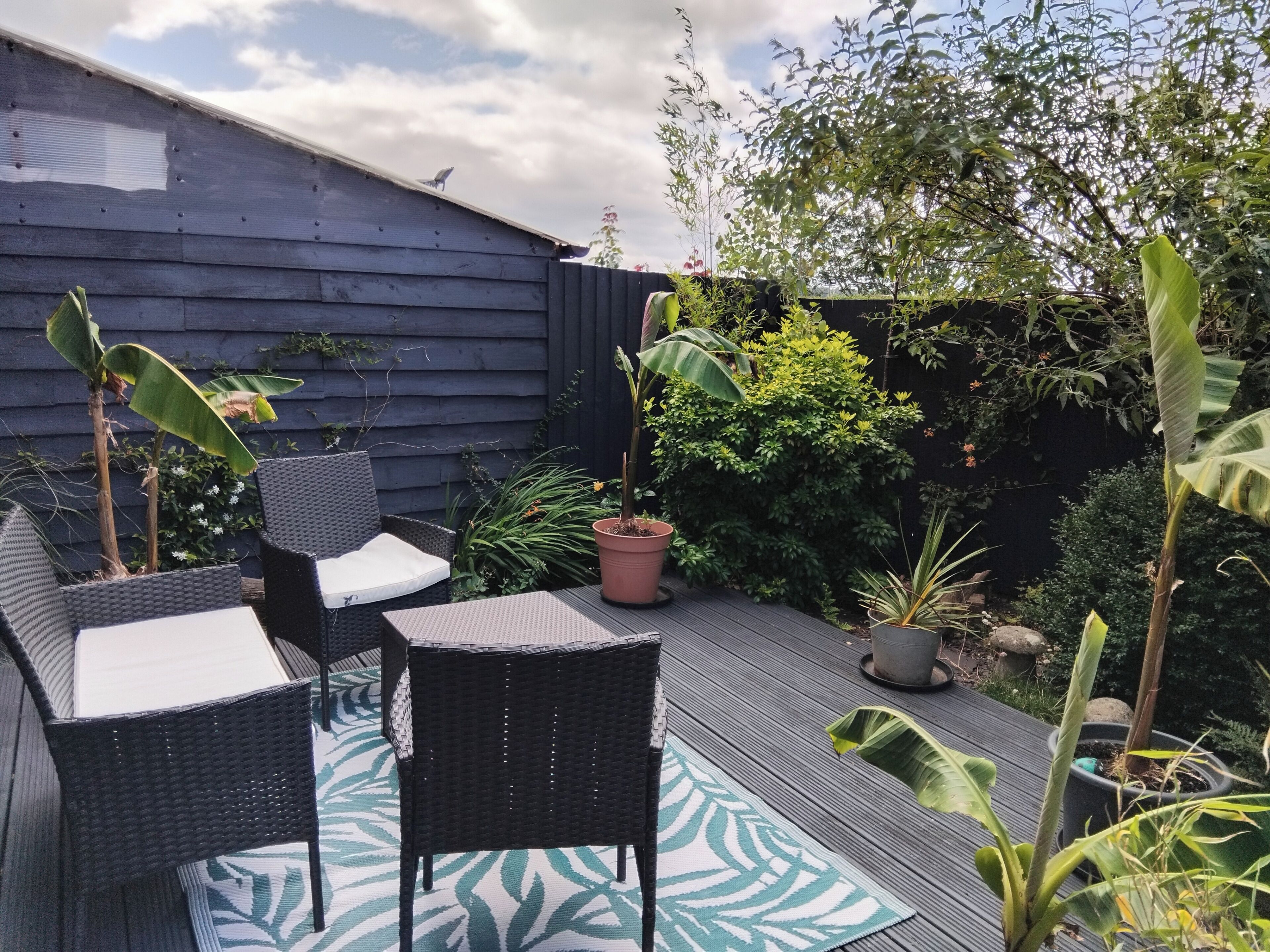 A deck with wicker furniture, a patterned mat, and various potted plants.