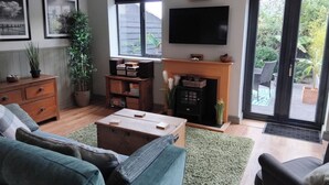 A living room with a fireplace, a television, and a large window. - 1-bed Apartment - Sleeps 2 & Private Parking (Llansantffraid-ym-Mechain)