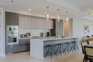 A modern kitchen with a central island, bar stools, stainless steel appliances, and pendant lighting.