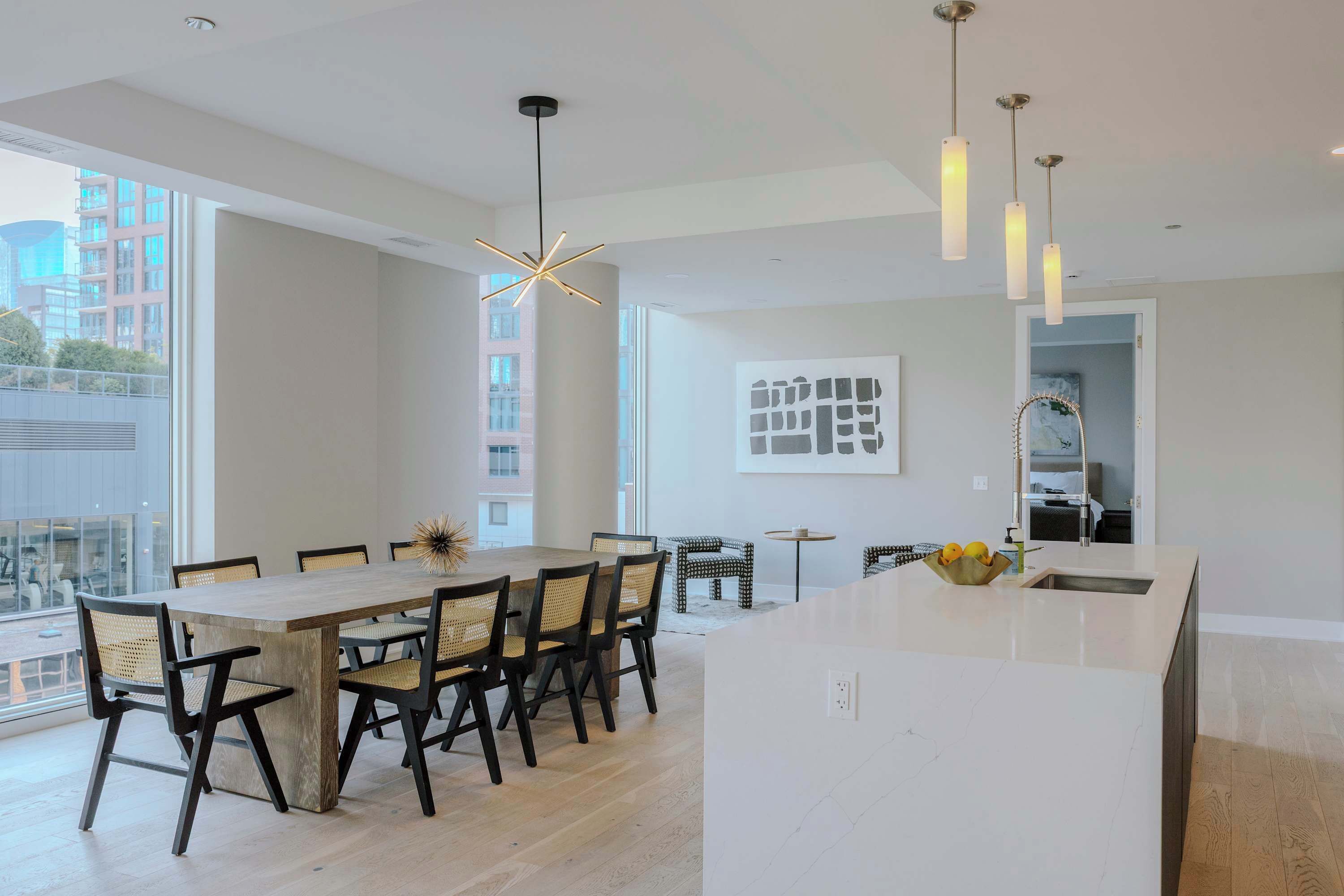 A modern kitchen with a large island, dining area with chairs, pendant lights, and a view of the city.