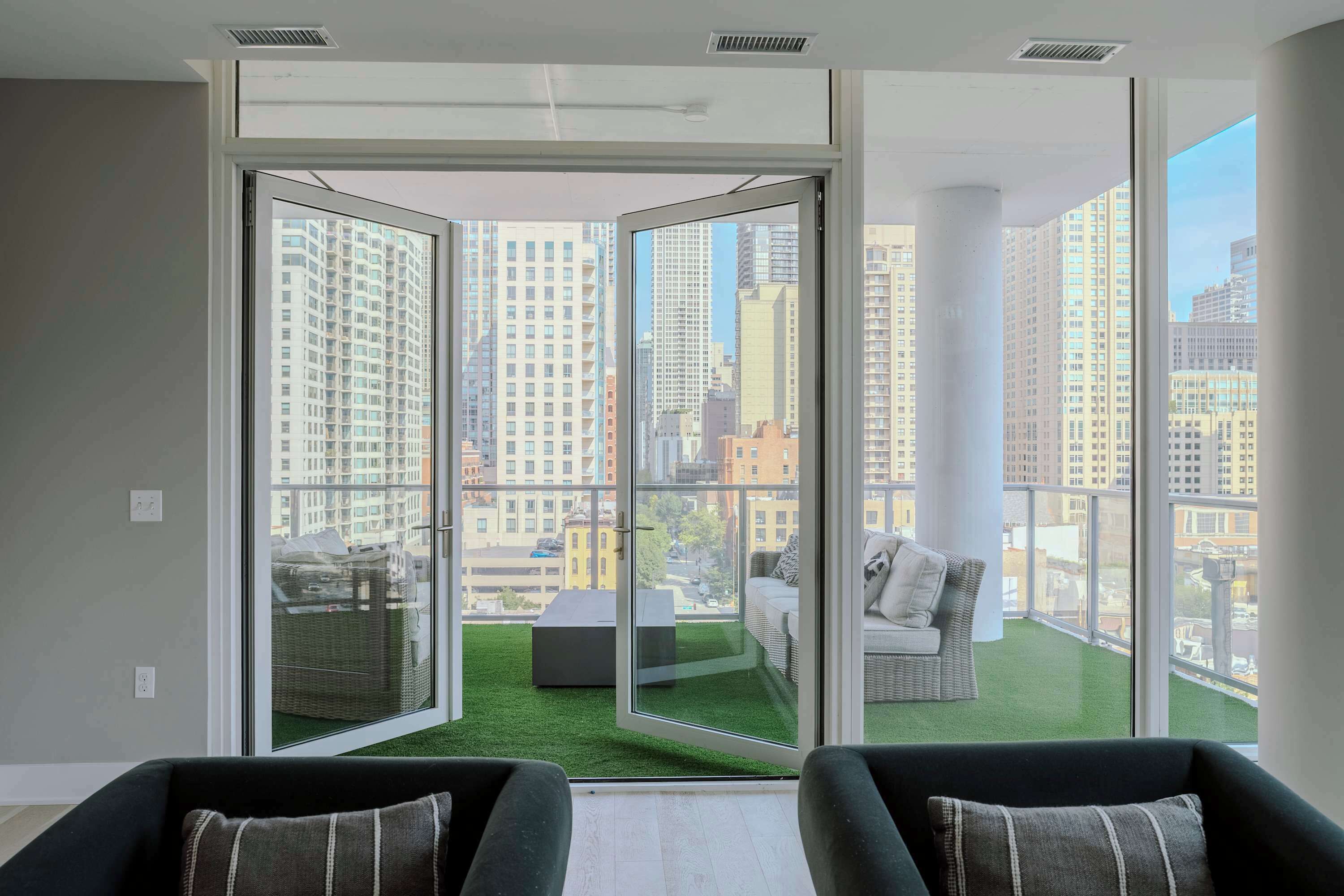 A modern apartment with large sliding glass doors, a balcony with artificial grass, and a city view.