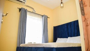 Un dormitorio con cama, cortinas, unidad de aire acondicionado y una lámpara en el techo.