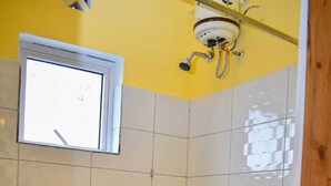 Un baño pequeño con inodoro, ventana y cabezal de ducha.