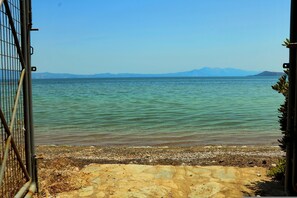 A view of a lake with mountains in the distance, a rocky shore, and a metal gate. - Ekatis Seacoast Nest (Lokroi)
