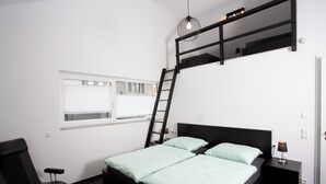 Ein Schlafzimmer mit Etagenbett, Schreibtisch, Stuhl und einem Fenster mit Jalousien.