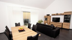Ein modernes Wohnzimmer mit einem Holzesstisch, schwarzen Stühlen, einem schwarzen Sofa, einem Fernseher und einem Weinkabinett.