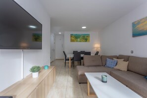 Ein modernes Wohnzimmer mit einem Flachbildfernseher, einer Couch, einem Esstisch mit Stühlen und einem Bild an der Wand.