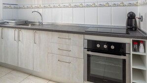 Una cocina moderna con armarios blancos, un lavamanos de acero inoxidable, una cafetera y un horno.