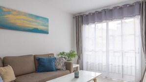 Una sala de estar moderna con un sofá color beige, una mesa de centro blanca y un ventanal con cortinas.