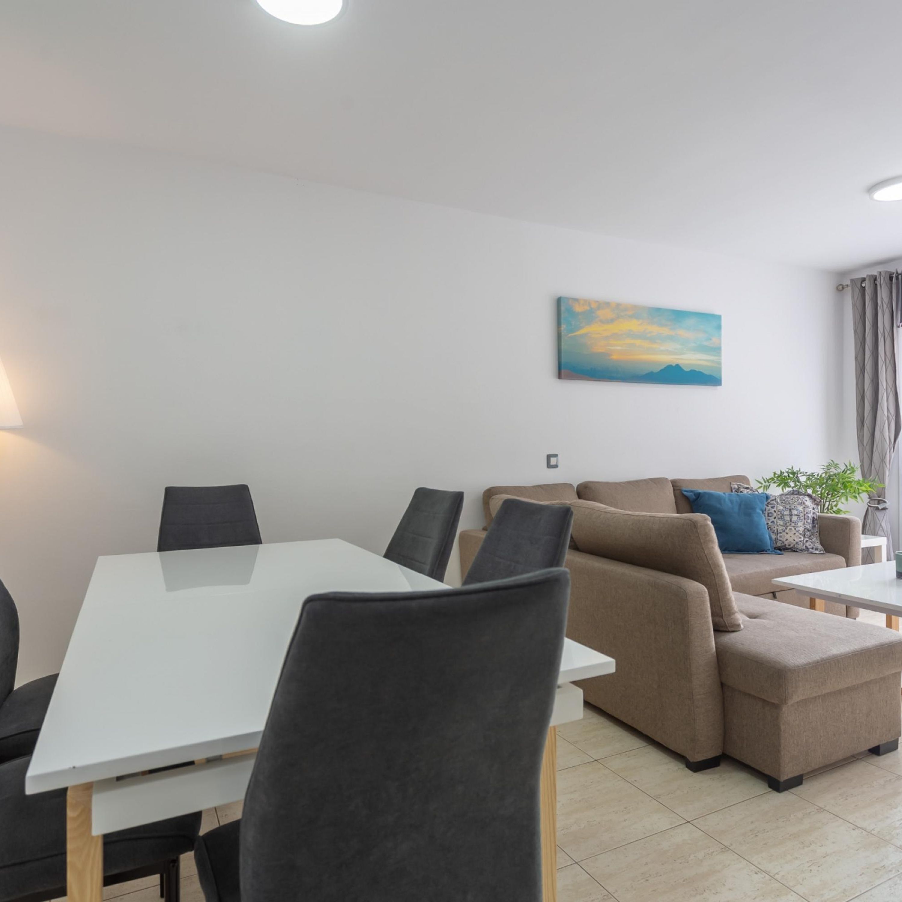 Un soggiorno moderno con un tavolo da pranzo bianco, sedie grigie, un divano beige e un quadro appeso al muro.