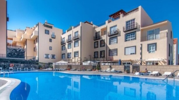 Una piscina con sillas de descanso y sombrillas, rodeada de edificios de varios pisos con balcones.