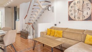 A living room with a sofa, a wooden table, a staircase, and a wall clock. - Aqua Vista 2 bed Penthouse With Great Views (Adeje)