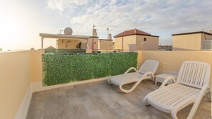 A rooftop terrace with two white lounge chairs, a green hedge, and a view of neighboring buildings. - Aqua Vista 2 bed Penthouse With Great Views (Adeje)