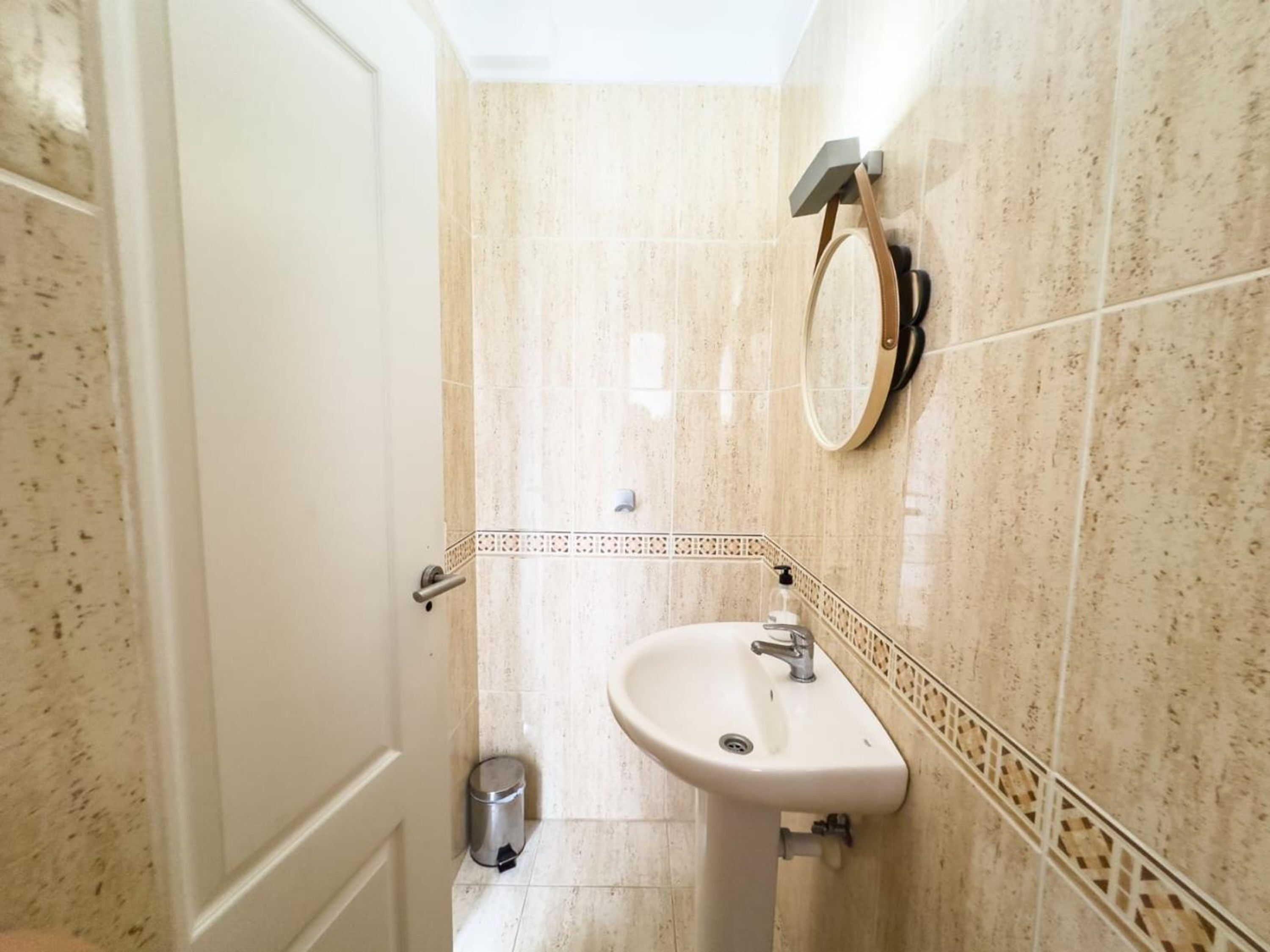 A bathroom with a white sink, a mirror, and a trash can.
