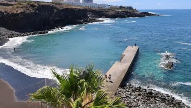 A coastal scene with a concrete pier extending into the ocean, surrounded by rocky terrain and palm trees. - Central 2bedroom 200m From Beach (Adeje)