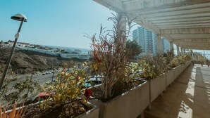 A covered outdoor area with concrete beams, potted plants, and a view of the sea and buildings in the distance. - Seaview Splendor 2 Bedroom Modern Comfort (Adeje)
